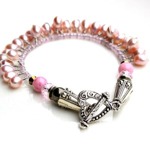 Puede incluir: Una pulsera delicada con perlas de agua dulce rosas y peque&ntilde;as cuentas rosas. La pulsera tiene un cierre de palanca plateado y detalles met&aacute;licos decorativos. Las perlas est&aacute;n dispuestas en un dise&ntilde;o en cascada.