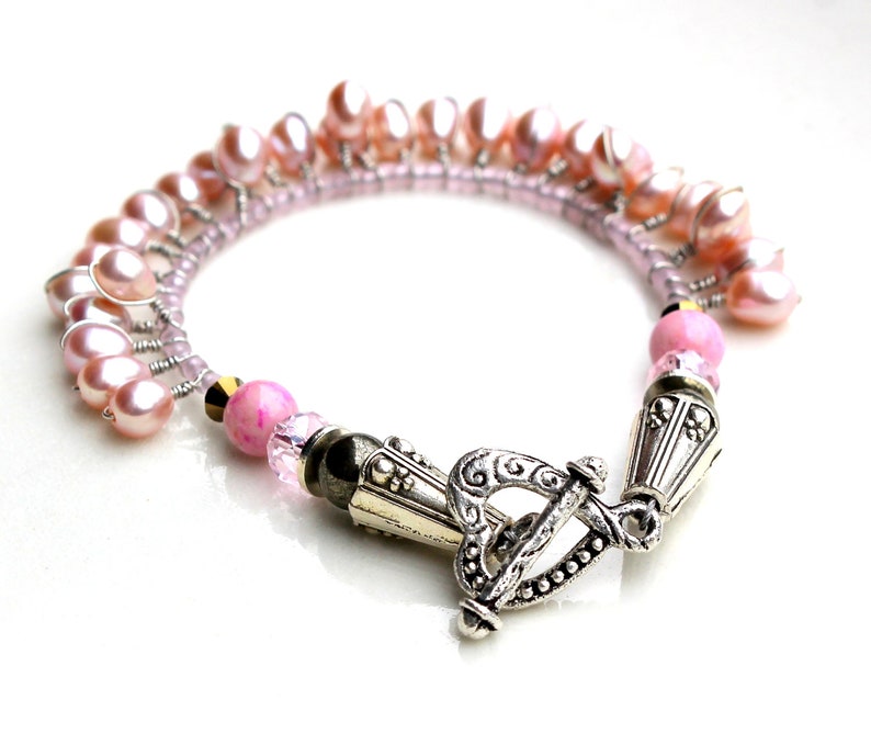 Puede incluir: Una pulsera delicada con perlas de agua dulce rosas y peque&ntilde;as cuentas rosas. La pulsera tiene un cierre de palanca plateado y detalles met&aacute;licos decorativos. Las perlas est&aacute;n dispuestas en un dise&ntilde;o en cascada.