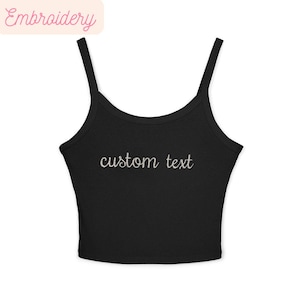 May include: Black crop top with thin straps and the embroidered text "custom text" in a cursive font. The top has a scoop neckline and is made of a soft, stretchy material. The word "Embroidery" is in a pink banner in the upper left corner.