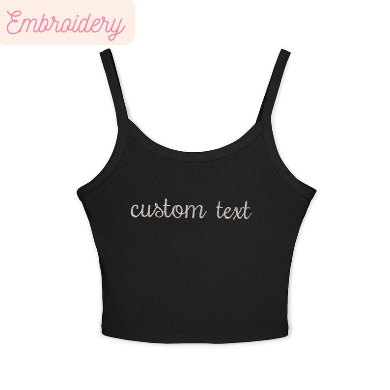 May include: Black crop top with thin straps and the embroidered text "custom text" in a cursive font. The top has a scoop neckline and is made of a soft, stretchy material. The word "Embroidery" is in a pink banner in the upper left corner.