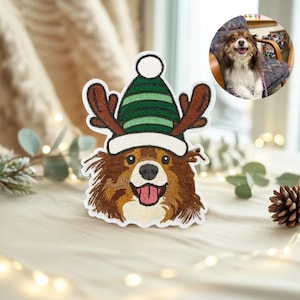 May include: Embroidered patch featuring a brown and white dog wearing a green and white striped hat with antlers. The dog has a pink tongue sticking out. A small photo of the dog is in the upper right corner.