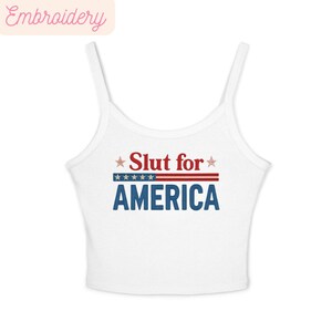 May include: White tank top with thin straps. The front features the text "Slut for AMERICA" in red, white, and blue, with stars and stripes design. The top is a casual style.