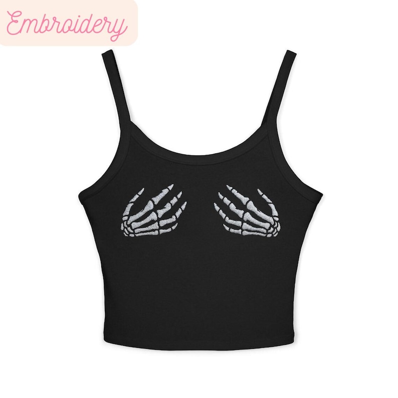 May include: Black camisole top featuring white embroidered skeleton hands. The top has thin straps and a scoop neckline. The word "Embroidery" is printed in a light pink colour in the upper left corner.
