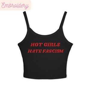 May include: Black camisole top with thin straps. The words "HOT GIRLS HATE FASCISM" are embroidered in red across the front. A casual garment.