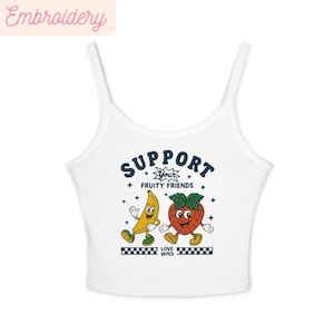 May include: White crop top featuring a cartoon banana and strawberry with arms and legs. The text "SUPPORT YOUR FRUITY FRIENDS" is above the fruit characters, and "LOVE WINS" is below. The word "Embroidery" is in the top left corner.