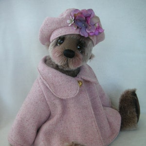May include: A plush teddy bear wearing a pink coat and a pink beret with purple flowers. The bear has brown fur and a black nose.