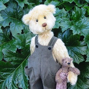 May include: A beige teddy bear wearing overalls and holding a smaller teddy bear. The larger bear has a brown nose and black eyes. The smaller bear is wearing a pink and white striped shirt. Both bears are standing on a white surface.