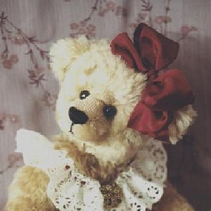 May include: A plush teddy bear with a cream-colored fur, wearing a white lace collar and a large red bow. The bear has a black nose and brown eyes.