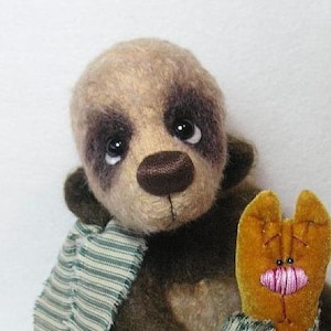 Puede incluir: Un oso de peluche marrón y beige con una bufanda a rayas verdes y blancas. El oso tiene ojos marrones y una nariz marrón. El oso sostiene un pequeño juguete de peluche naranja y marrón con una boca rosa.