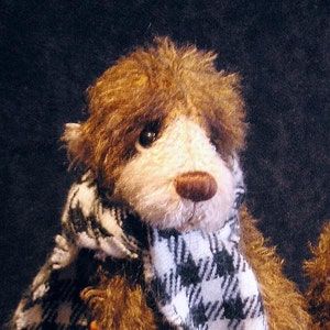 May include: A brown and white teddy bear wearing a black and white houndstooth scarf. The bear has a soft, fluffy face with a black nose and brown eyes.