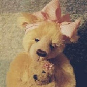 May include: A plush teddy bear with a large pink bow on its head and a smaller teddy bear clutched in its arms. The larger bear has a light brown fur and a pink headband. The smaller bear has a pink flower.
