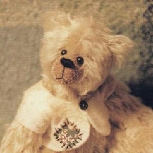 May include: A plush teddy bear with a white fur coat and a brown nose. The bear is wearing a white collar with a button and a floral patch.