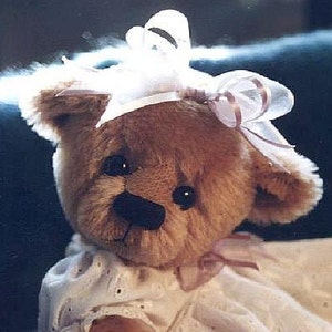 May include: A brown teddy bear wearing a white and pink bow. The bear is wearing a white dress with lace trim.