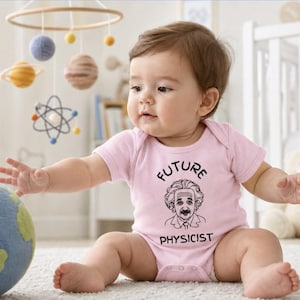 May include: A light pink baby bodysuit featuring a black graphic print of Albert Einstein with the text FUTURE PHYSICIST arched above and below the portrait. The garment has short sleeves, a round neckline, and snap closures at the bottom.