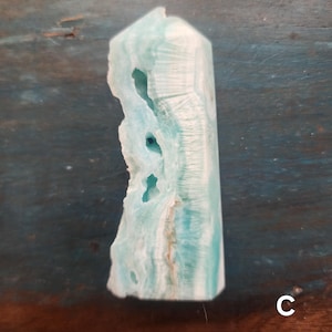 May include: A light blue and white crystal tower with a rough, textured edge. The crystal has a polished, smooth surface on the other sides. The crystal is a light blue color with white and brown streaks.