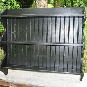 May include: Black wooden wall shelf with three shelves. The shelf has a scalloped edge and is made of wood planks.