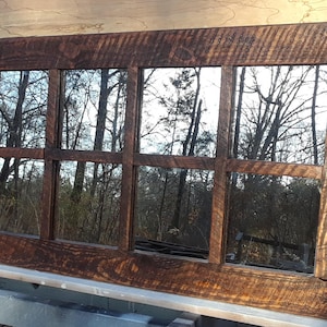 May include: A rustic wooden framed mirror with nine panes, reflecting a view of trees and a forest. The frame is dark brown with a distressed finish.