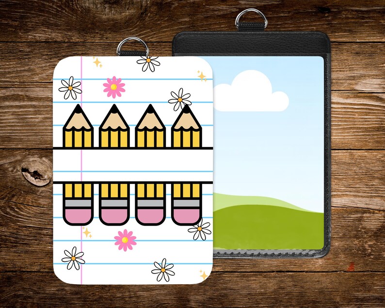 May include: Two ID badge holders. One features a white background with a pencil and eraser design, blue lines, and flower accents. The other is a black leather-like holder with a landscape image. Both have a silver ring for attachment.