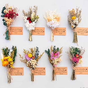 Puede incluir: Nueve peque&ntilde;os ramos de flores secas de varios colores, atados con hilo. Cada ramo tiene una peque&ntilde;a tarjeta con un mensaje de San Valent&iacute;n y un nombre. Los ramos est&aacute;n dispuestos sobre un fondo blanco.