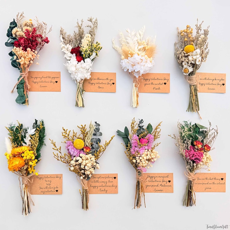 Puede incluir: Nueve peque&ntilde;os ramos de flores secas de varios colores, atados con hilo. Cada ramo tiene una peque&ntilde;a tarjeta con un mensaje de San Valent&iacute;n y un nombre. Los ramos est&aacute;n dispuestos sobre un fondo blanco.