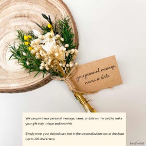 Puede incluir: Un peque&ntilde;o ramo de flores secas con flores verdes, amarillas y blancas, atado con hilo. Una etiqueta marr&oacute;n con el texto "your personal message, name, or date" est&aacute; adjunta. El ramo descansa sobre una rodaja de madera.