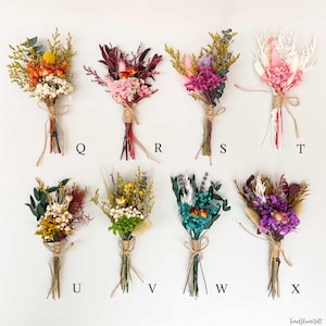 Puede incluir: Una colecci&oacute;n de ocho peque&ntilde;os ramos de flores secas, cada uno atado con hilo. Los ramos presentan una variedad de colores, incluyendo naranja, rosa, morado, blanco, amarillo y turquesa. Cada ramo est&aacute; etiquetado con una letra de la Q a la X.