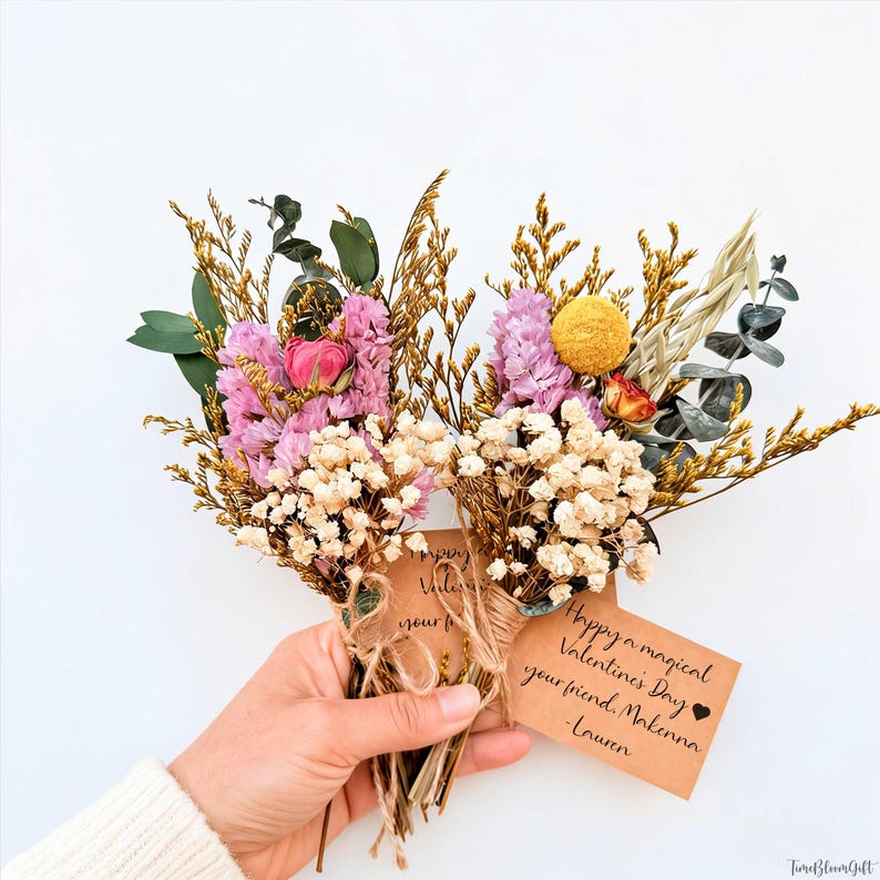 Puede incluir: Dos ramos de flores secas con flores rosas, amarillas y blancas, atados con hilo y una tarjeta peque&ntilde;a. La tarjeta dice "Happy a magical Valentine's Day your friend, Malenna - Lauren". Los ramos se sostienen en una mano.