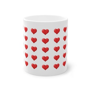 Puede incluir: Taza de cerámica blanca adornada con un patrón repetido de corazones rojos brillantes. Los corazones están espaciados uniformemente en la superficie de la taza, creando un diseño alegre. Ideal para café, té o cualquier bebida.