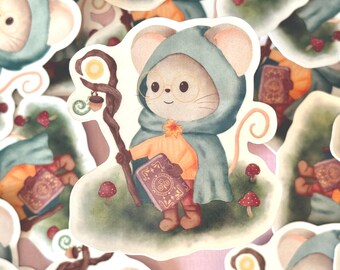 Puede incluir: Una pegatina caprichosa con un personaje de ratón vestido con una capa con capucha verde azulado y gafas redondas, sosteniendo un bastón con un orbe brillante y un libro. El ratón lleva un suéter naranja y está de pie sobre un parche cubierto de hierba con setas.