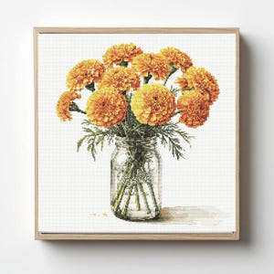 Pode incluir: Uma obra de arte em ponto cruz de um buquê de flores de calêndula laranja em um frasco de vidro transparente. As flores têm formato esférico e são cercadas por folhas verdes. A obra de arte é emoldurada em uma moldura de madeira marrom clara.