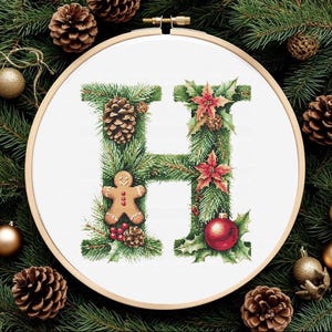 May include: Cross-stitch embroidery of the letter "H" decorated with Christmas elements. The design includes pine needles, pine cones, red poinsettias, a gingerbread man, and a red ornament, all set within a wooden embroidery hoop.