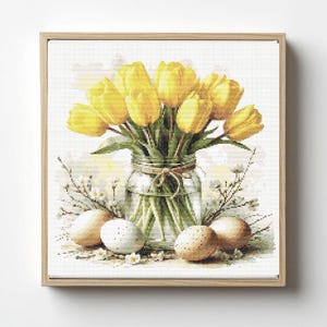Könnte beinhalten: Gerahmter Kunstdruck mit einem Strauß gelber Tulpen in einem Glasgefäß, das mit Bindfaden gebunden ist. Mehrere gesprenkelte Eier und kleine weiße Blüten umgeben das Gefäß. Helles, frühlingshaftes Motiv.