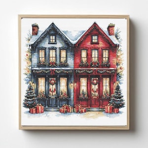 May include: A framed cross-stitch artwork depicts two adjacent houses, one blue and one red, decorated for Christmas. Each house has lit windows, wreaths, and presents. Snow and Christmas trees complete the festive scene.
