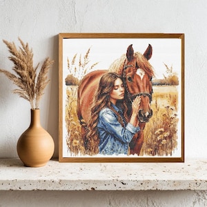 以下が含まれることがあります： デニムジャケットを着た女性が、茶色の馬を抱きしめている様子を描いた、額入りのクロスステッチアート。木製のフレームに入っており、ニュートラルな色使いです。