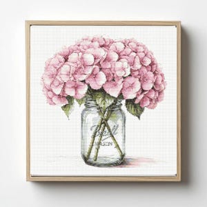 May include: A framed cross-stitch artwork featuring a bouquet of pink hydrangeas in a clear glass mason jar. The jar has the word "Mason" printed on it. The artwork is set against a white background.