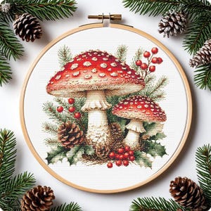Może przedstawiać: Haft krzyżykowy przedstawiający dwa czerwono-białe grzyby w kropki, otoczone igłami sosny, ostrokrzewem i szyszkami, umieszczony w drewnianej tamborku. Projekt ma szczegółowy, realistyczny styl, z świątecznym, sezonowym motywem.