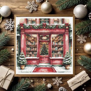 May include: A framed cross-stitch pattern depicting a red storefront with large glass windows filled with bookshelves, a central door with a Christmas tree, a red welcome mat, and two small potted Christmas trees on either side of the entrance.