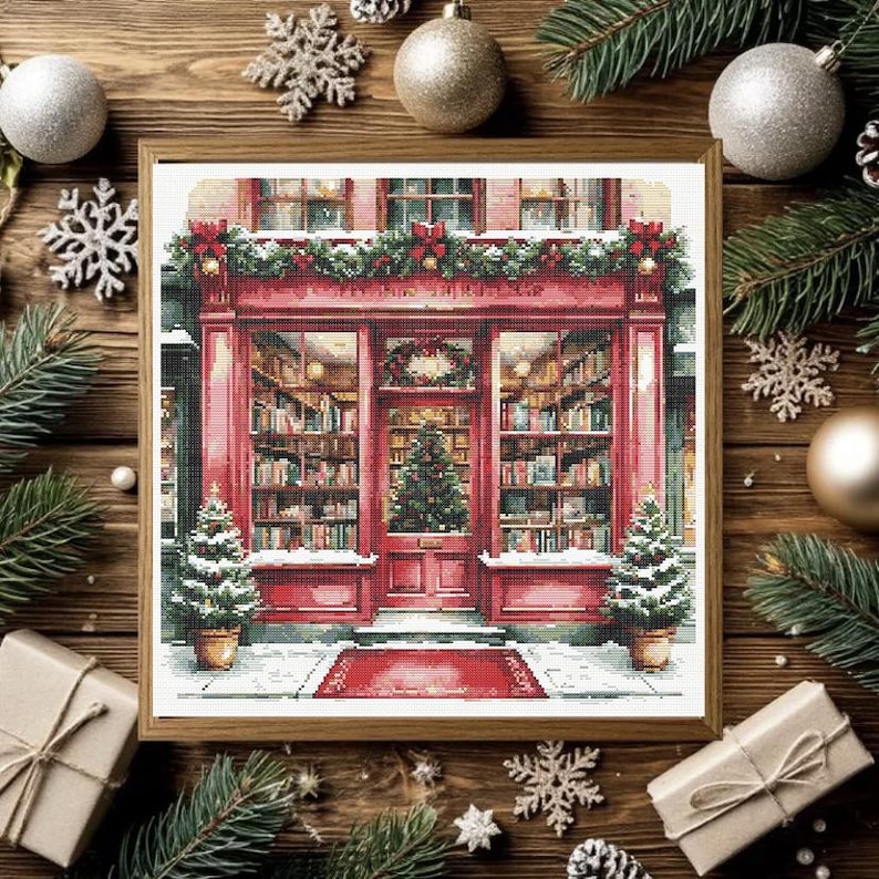 May include: A framed cross-stitch pattern depicting a red storefront with large glass windows filled with bookshelves, a central door with a Christmas tree, a red welcome mat, and two small potted Christmas trees on either side of the entrance.