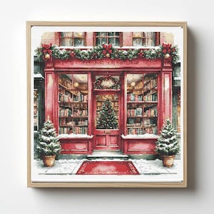 Puede incluir: Un bordado enmarcado que representa una escena festiva de una librería. El edificio rojo tiene grandes ventanales que muestran estanterías llenas de libros. Un árbol de Navidad se encuentra dentro de la puerta, y dos árboles en macetas flanquean la entrada. La nieve y las decoraciones adornan el edificio.