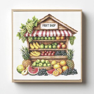 Puede incluir: Un bordado en punto de cruz de un puesto de frutas de madera con un toldo a rayas rojas y blancas. El letrero dice FRUIT SHOP. Los estantes están llenos de varias frutas, incluyendo uvas verdes, plátanos amarillos, manzanas y piñas.