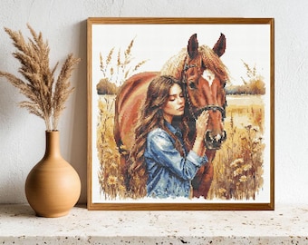 May include: A square framed cross-stitch pattern depicting a person with long brown hair wearing a blue denim shirt, standing in a golden field next to a brown horse with a white blaze on its forehead, surrounded by tall grasses and wildflowers.