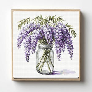 May include: A framed print featuring a cross-stitch design of wisteria flowers in a mason jar. The flowers are a gradient of purple and lavender, with green leaves. The jar is clear, and the frame is light brown.