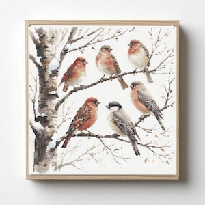 May include: A square cross-stitch embroidery piece in a light wood frame depicting five small birds perched on bare, snow-dusted tree branches. The birds feature shades of brown, red, and grey, set against a white background with a birch tree.