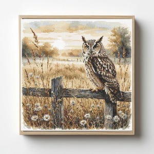 Peut inclure: Une broderie au point de croix carrée représentant un hibou brun et blanc perché sur un poteau de clôture en bois patiné. La scène montre un coucher de soleil doré sur un champ d'herbes hautes et de fleurs sauvages, encadrée de bois clair.