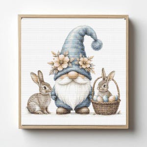May include: A framed print featuring an Easter gnome with a blue hat and a long white beard, flanked by two rabbits. One rabbit sits beside the gnome, and the other is in a basket with Easter eggs. The artwork has a watercolor style.