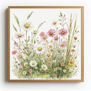 May include: A framed cross-stitch of a wildflower meadow. The artwork features white daisies with yellow centers, pink and yellow wildflowers, and tall green and tan grasses. The artwork is in a light brown wooden frame.