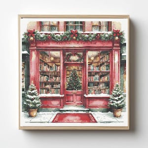 Puede incluir: Un patrón de punto de cruz cuadrado que representa un escaparate rojo con grandes ventanales llenos de libros. La tienda está decorada con guirnaldas verdes, lazos rojos y un árbol de Navidad central. Dos árboles nevados flanquean la puerta.