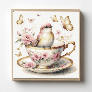 May include: A framed cross-stitch artwork featuring a bird perched inside a floral teacup. The teacup and saucer are adorned with pink flowers and gold trim. Butterflies flutter around the bird, adding to the delicate, vintage aesthetic.