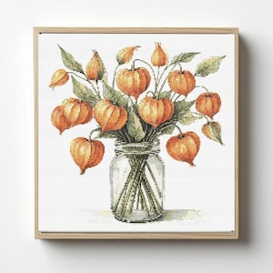 Könnte beinhalten: Ein Kreuzstich-Kunstwerk eines Bouquets aus orangefarbenen chinesischen Lampionblumen in einem durchsichtigen Glas. Die Blumen haben eine markante Laternenform und sind von grünen Blättern umgeben. Das Kunstwerk ist in einem hellbraunen Holzrahmen gerahmt.
