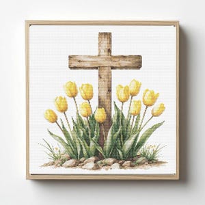 May include: A framed cross-stitch picture showing a wooden cross and yellow tulips. The cross is made of weathered wood, and the tulips are in full bloom with green leaves. The artwork is set against a white background.